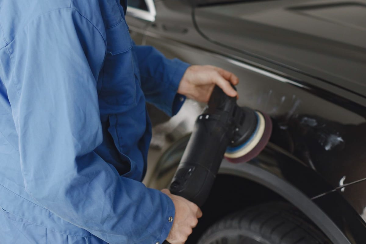 A professional detailing bay with a car under even overhead lighting, polishing equipment ready at the side.