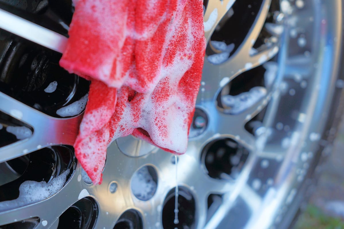 Detailing supplies on a workbench: spray bottles, a polishing pad, and folded microfiber cloths.