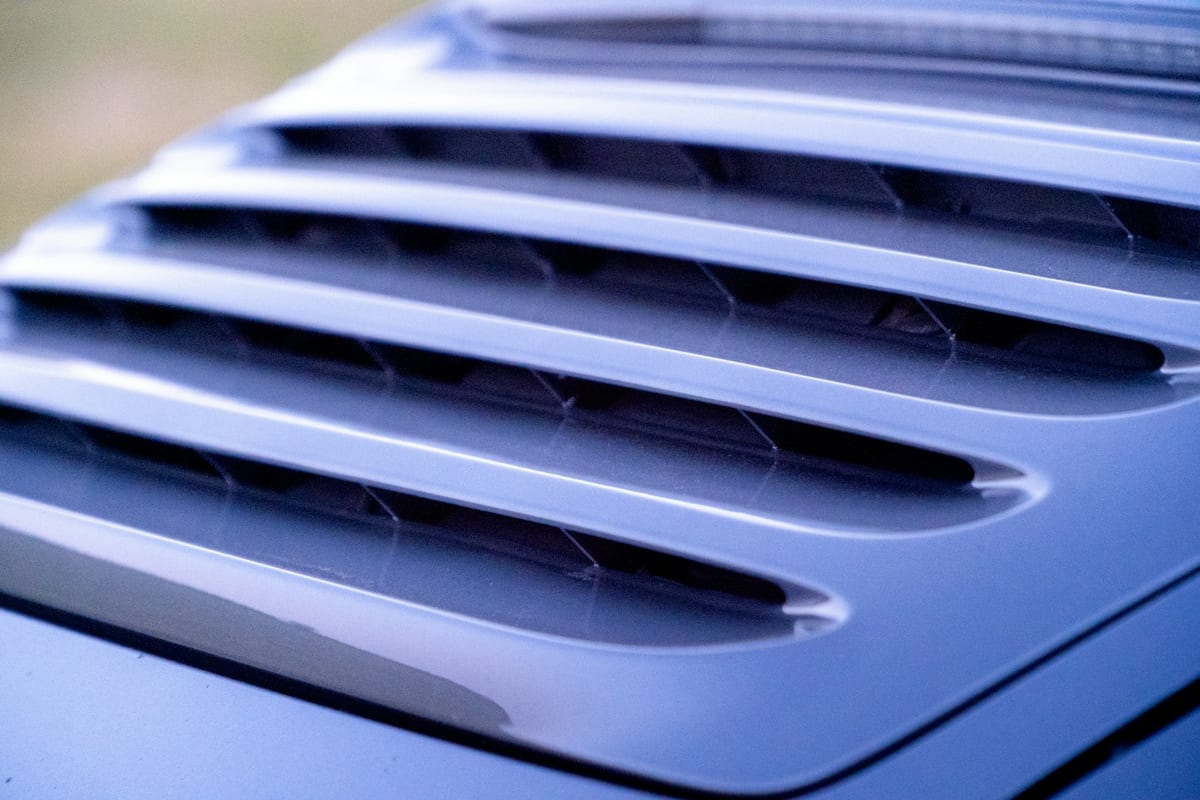 A close, abstract view of a car body panel, its curve catching a long highlight of reflected light.