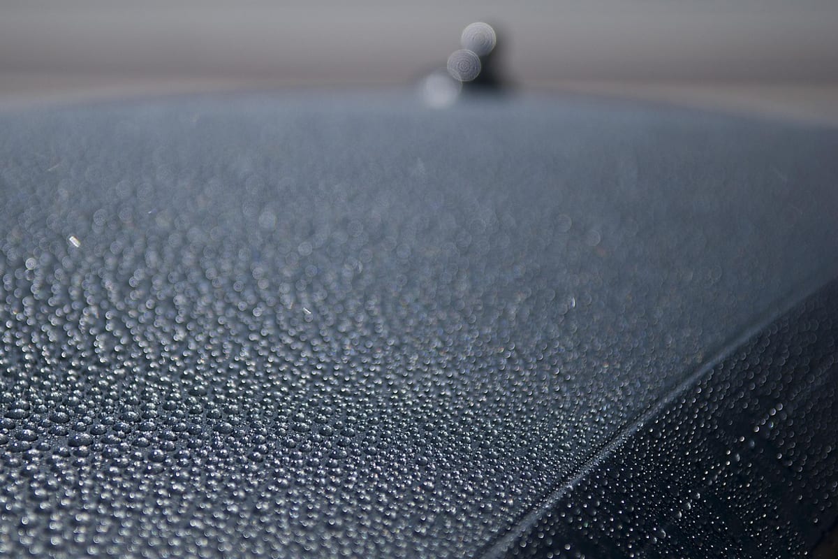 Extreme close-up of dense, fine water droplets covering the curved edge of a coated car's dark roof panel.