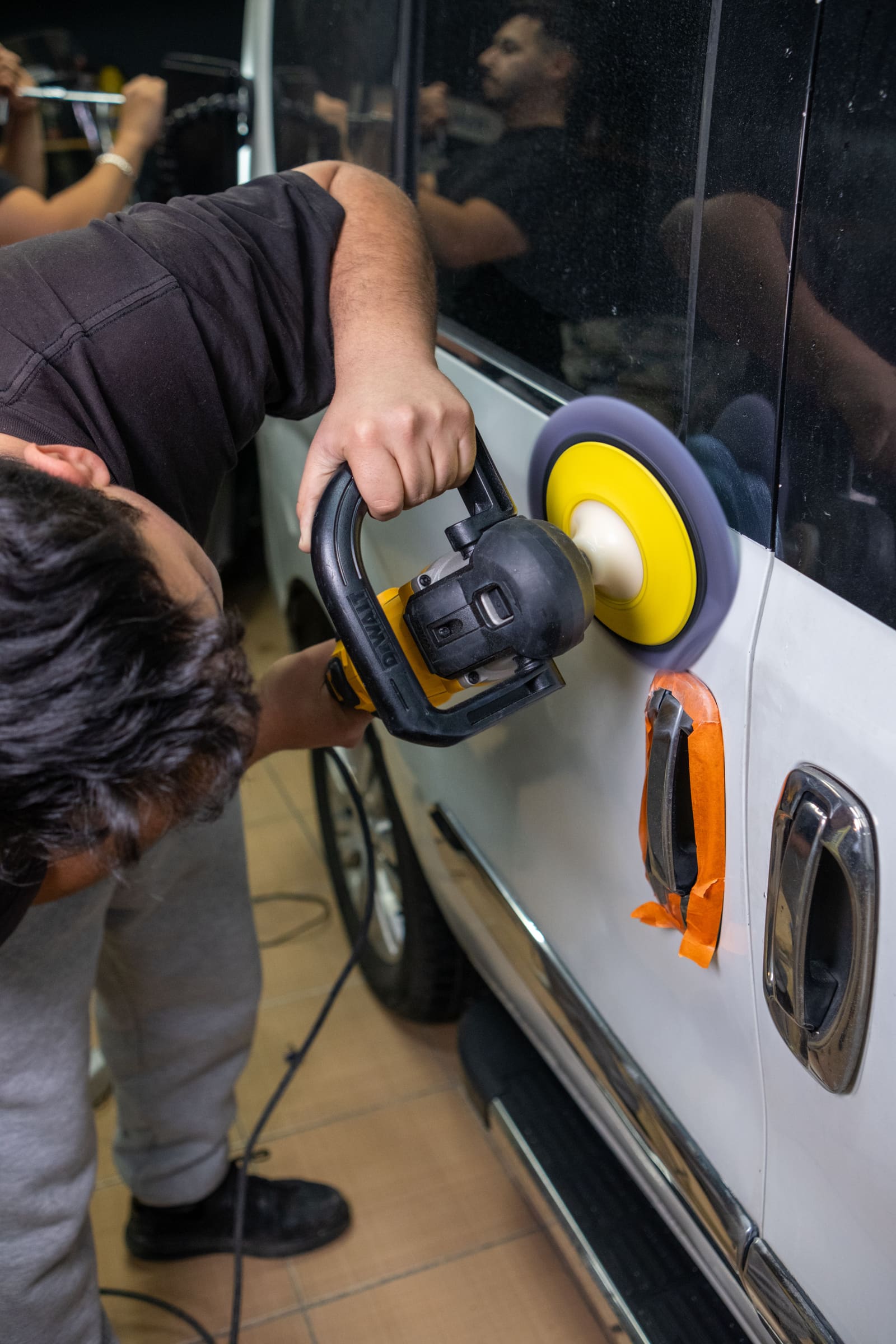 A technician using an electric buffer to polish a car door, illustrating the same buff-and-seal step used to finish a restored headlight.