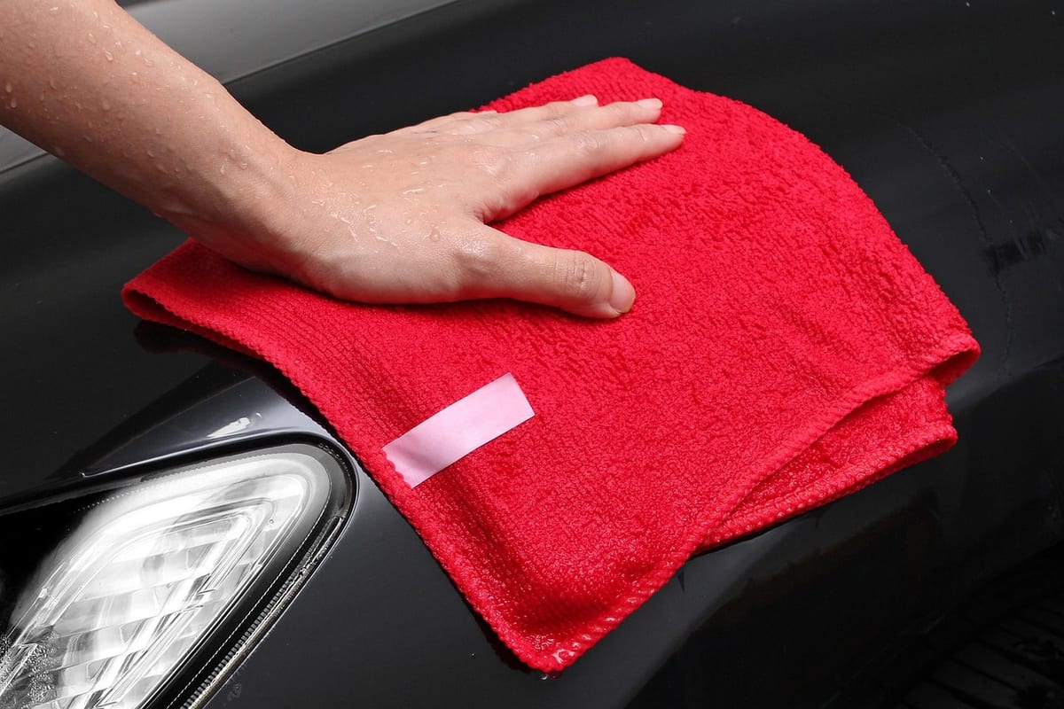 A hand wiping down a dark car panel with a red microfiber cloth during prep.