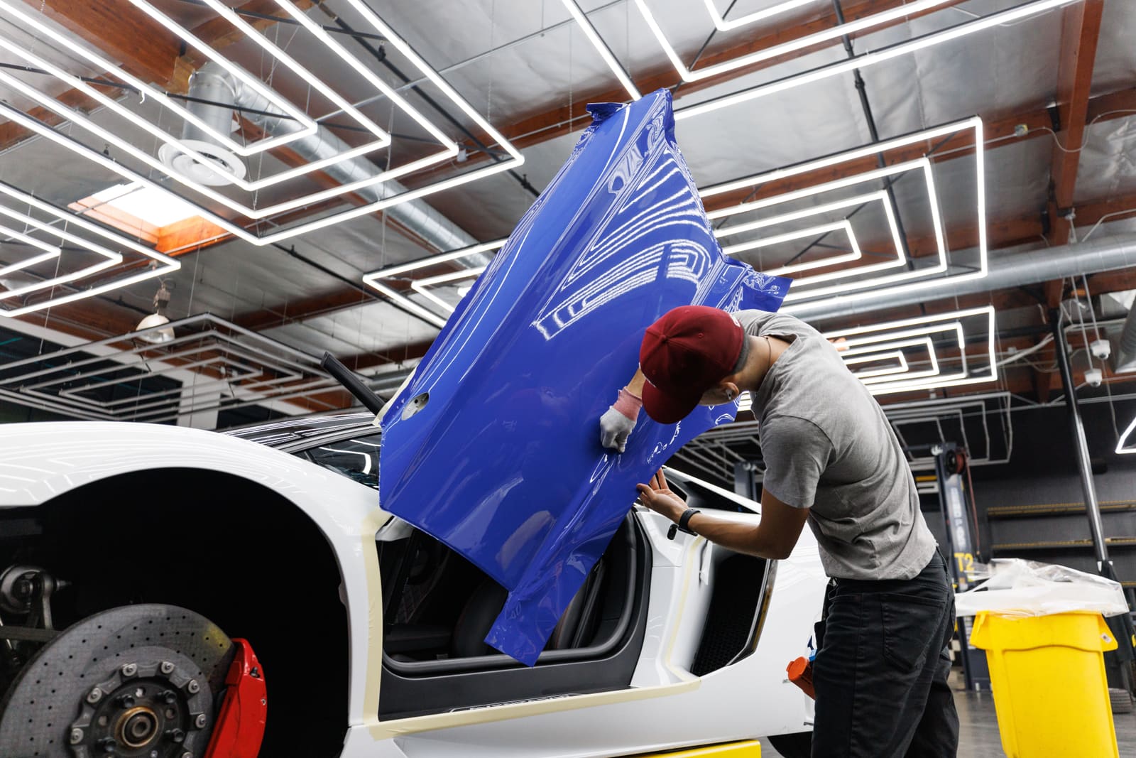 An auto mechanic applying a blue vinyl wrap film to a car door in a modern garage.