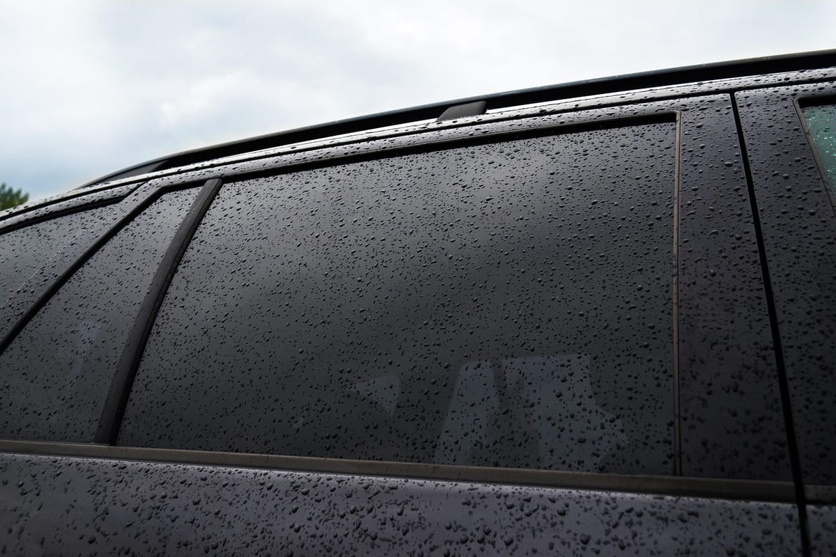 Rain beading and sheeting off the dark tinted side glass of a car.