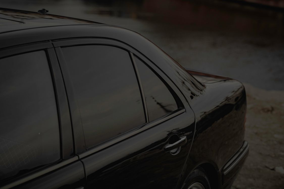 Close-up of a black Mercedes with visibly dark tinted rear and side windows, parked beside a calm river.